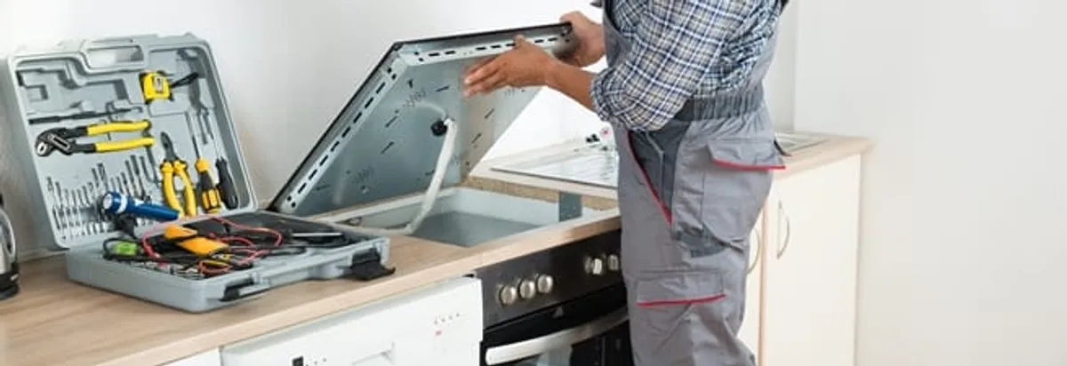 Cooktop repair technician lifting a built-in stovetop for service in Erie, PA
