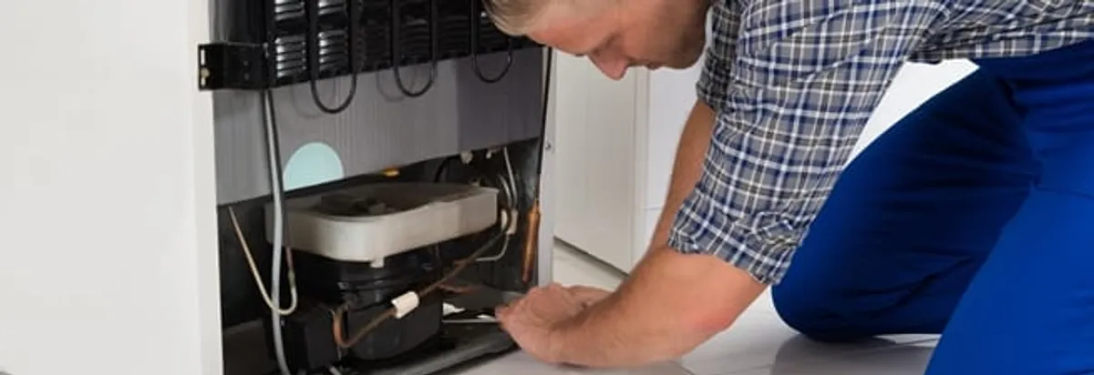Refrigerator repair technician servicing the compressor and condenser area in Erie, PA