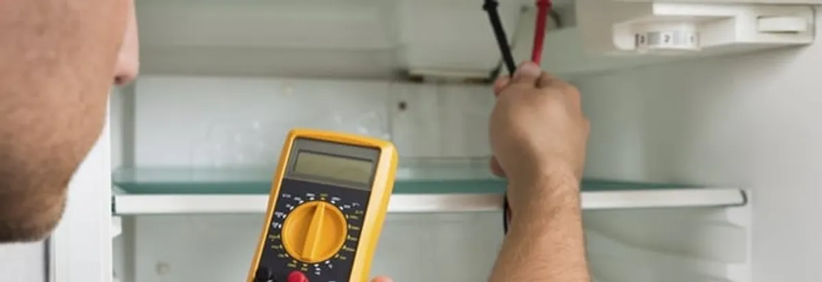 Refrigerator repair technician testing electrical components with a multimeter in Erie, PA